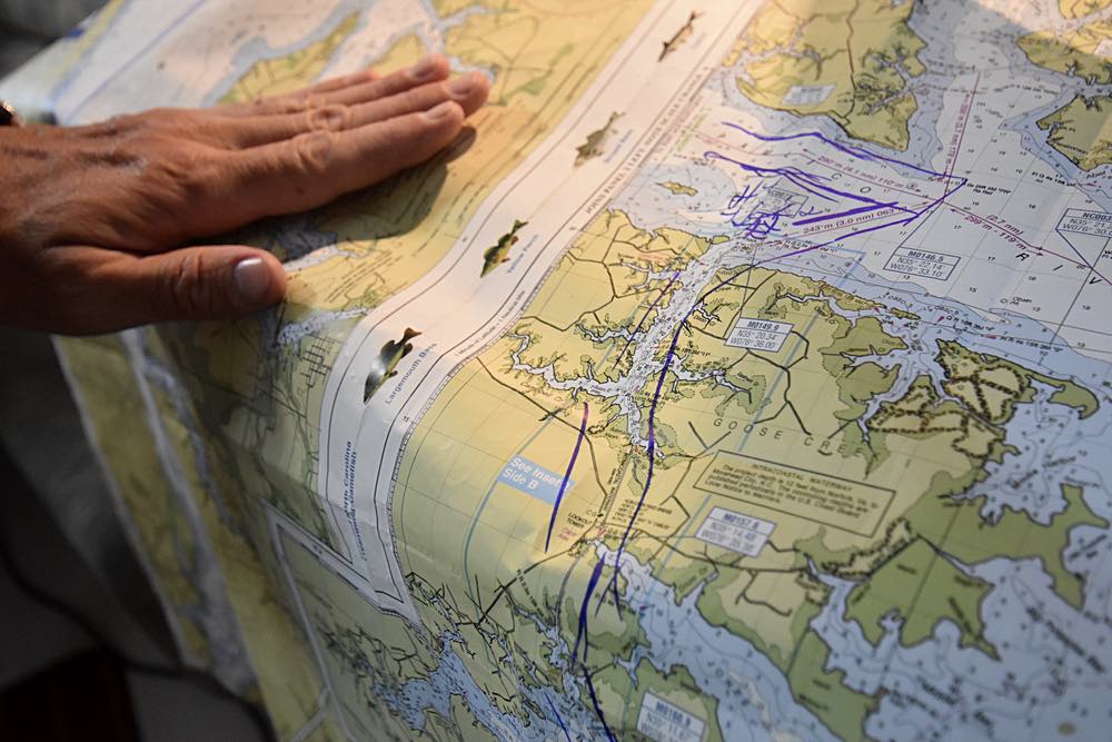 A hand holds a nautical chart flat on the table. Purple marks show the boat's route.