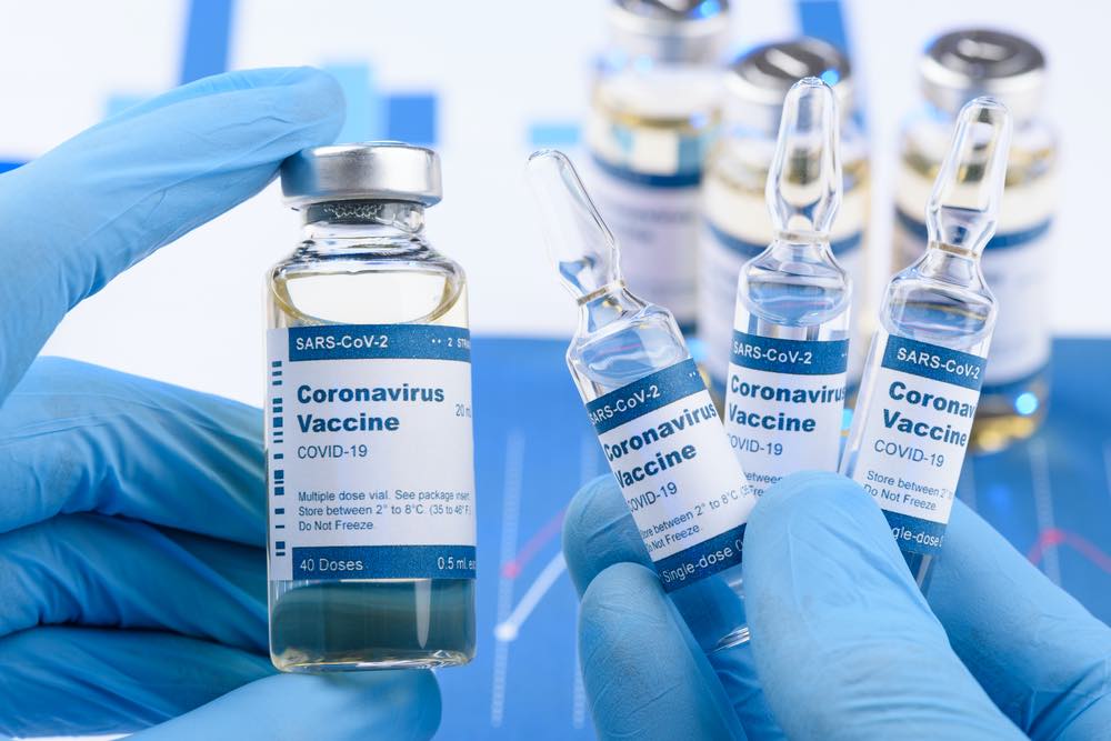 blue gloved hands hold vials of covid vaccine
