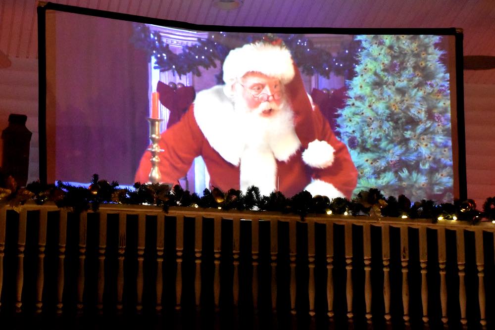 A flexible screen shows a projection of Santa looking over the balcony