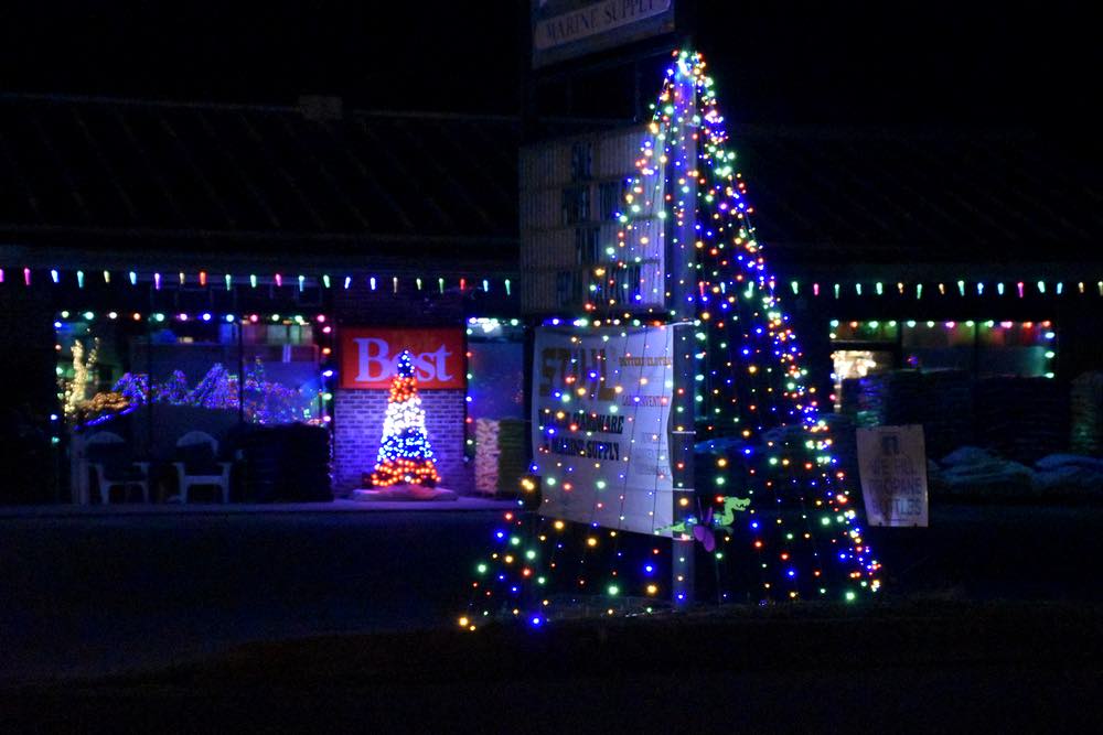 Two lit trees in the front of Village Hardware; one along the road and one at the building.
