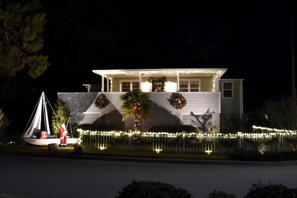 A raised cottage with white lights and a fishing Santa in the front yard