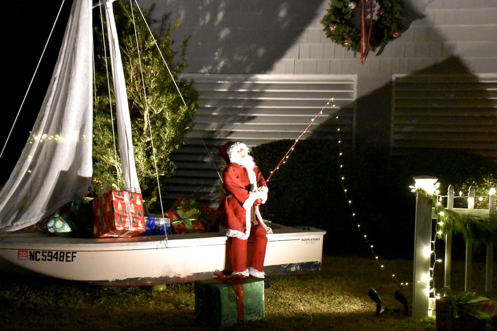An animatronic Santa sits on a fishing boat full of presents, casting a line of lights for more presents.
