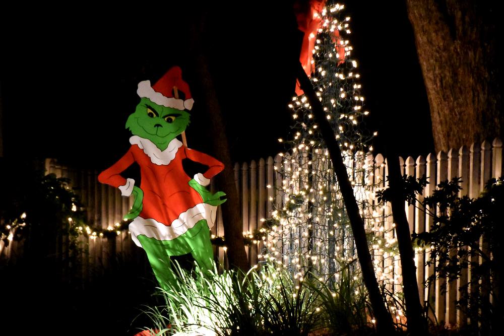 a life-size Grinch cutout stands next to a Christmas tree