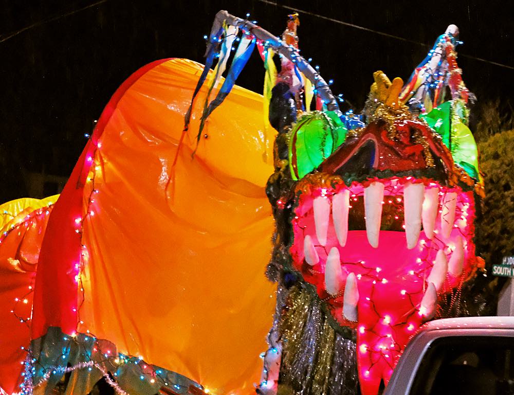 A large colorful parade dragon, lit from within by lights, shows it's teeth to the camera.