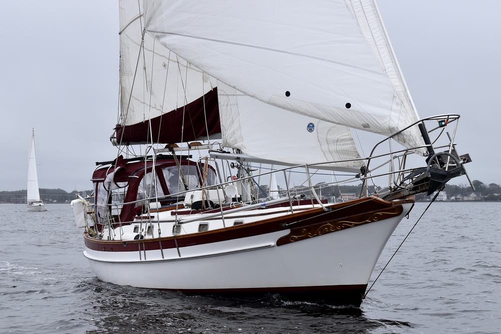 A white hulled sailing vessel with full sails and maroon canvas, passes by.