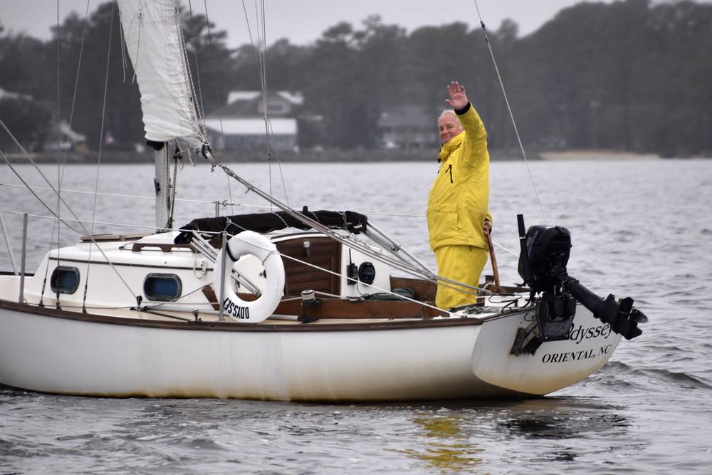 A man in yellow foul weather gear waves from a boat named Odyssey.