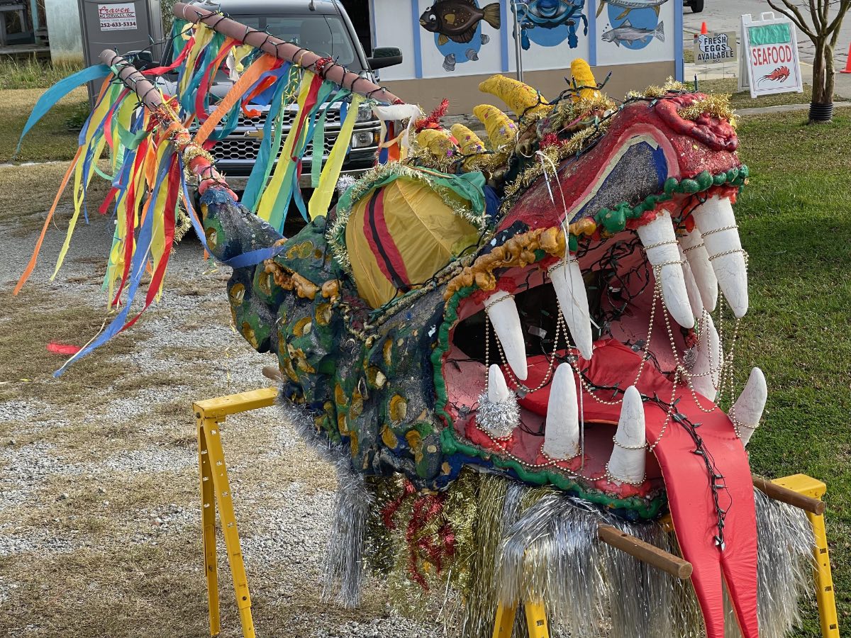 During the day, a large yellow, orange and red cloth dragon head sits on saw horses. Strings of light are wrapped around the teeth and draped over the tongue.
